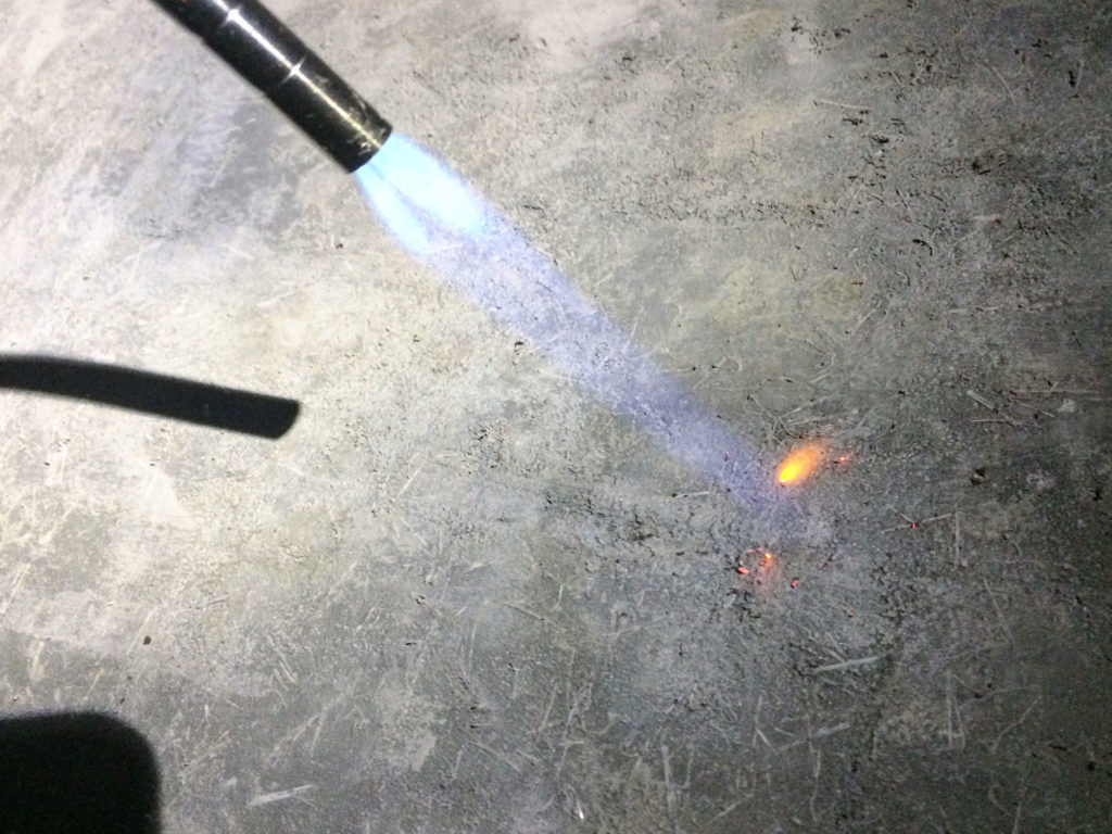 A propane hand torch burns plastic fibers from concrete surface. 